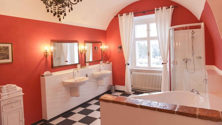 Badezimmer, © Schlosshotel Mailberg / point of view Elegantes Badezimmer mit roten Wänden, zwei Waschbecken, Badewanne, Dusche und Kronleuchter.