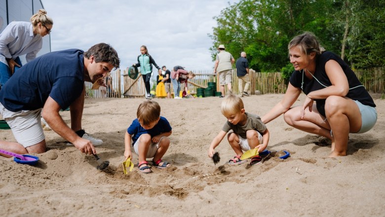 Viel Action im Forscherpark, © Fossilienwelt Familien graben im Sand nach Fossilien in einem Freilichtmuseum.