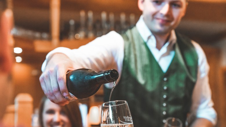 Andreas Simayr, © Matthias Auer Ein Mann in traditioneller Kleidung schenkt Wein in ein Glas ein.