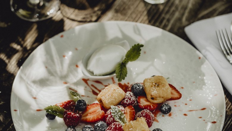 Gebackener Topfen mit marinierte Beeren & Joghurteis, © Niederösterreich Werbung/Sophie Menegaldo Ein Dessertteller mit gebackenem Topfen, marinierten Beeren und Joghurteis, dekoriert mit Minzblättern, auf einem Holztisch.