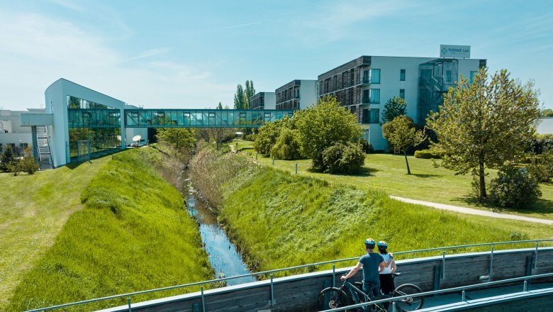 Therme Laa & Hotel, © Therme Laa / Pflanzl Media Two cyclists on a bridge in front of the Therme Laa & Hotel.
