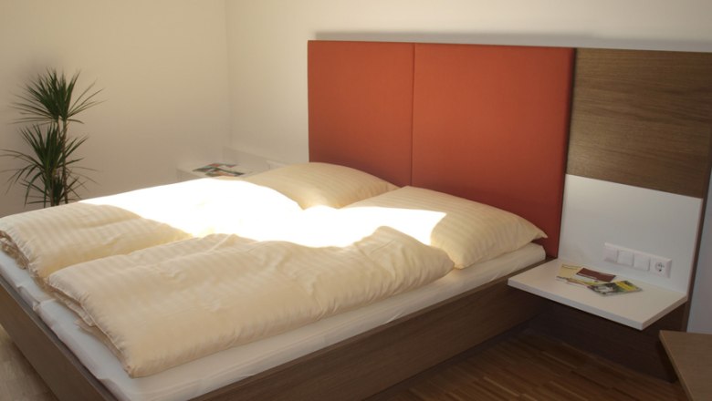 Gästezimmer, © Wolfgang Rieder Modernes Gästezimmer mit Doppelbett, rotem Kopfteil und Pflanzen.