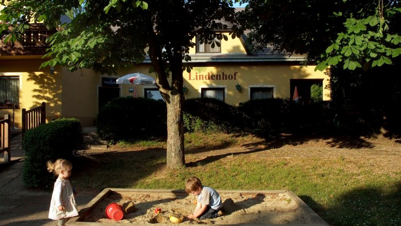 Lindenhof, © Seymannfilm Zwei Kinder spielen im Sandkasten vor einem Gebäude mit der Aufschrift 'Lindenhof'.