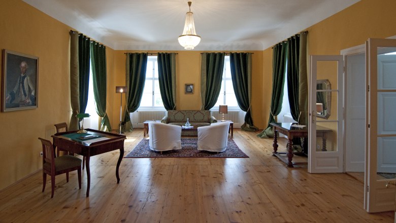 Hochzeitssuite, © Schlosshotel Mailberg / point of view Elegantes Zimmer mit Holzboden, grünen Vorhängen, zwei Sesseln, einem Sofa und einem Schreibtisch. Ein Kronleuchter hängt von der Decke.