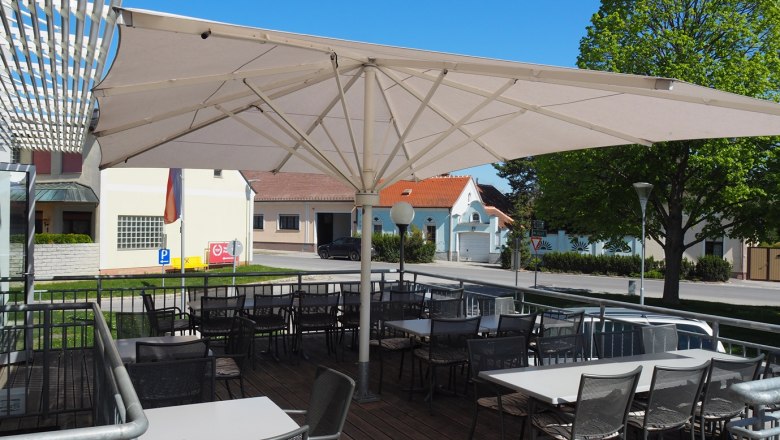 Terrasse Restaurant Hacker´s, © Restaurant Hacker's Terrasse eines Restaurants mit Sonnenschirm und leeren Tischen und Stühlen, im Hintergrund eine Straße und Gebäude.