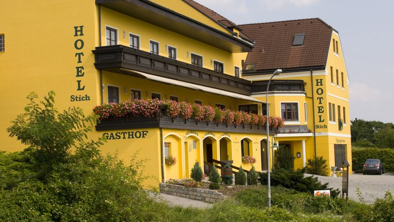 Hotel Stich, © Familie Stich Gelbes Hotelgebäude mit Blumen auf dem Balkon.