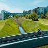 Two cyclists on a bridge in front of the Therme Laa & Hotel.