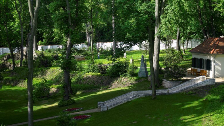 A well-kept garden with trees, lawns and a small building with a terrace.